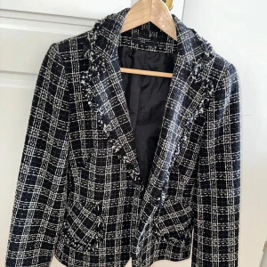 Rutig svartvit kavaj och kjol från Pourquoi Pas - Snyggt set med kavaj och kjol i svartvitt rutigt mönster från Pourquoi Pas. Kavajen har fransiga kanter och klassisk krage, kjolen är rak och matchar perfekt. Tjockare tyg med struktur, perfekt för dig som gillar preppy och trendig stil.