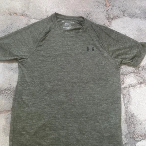 Under armour T-shirt  - Säljer en gråmelerad tech t-shirt från Under Armour med klassisk logga på bröstet och nacken. Den är helt ny utan prislapp och jätte bekväm även snygg till sommaren 