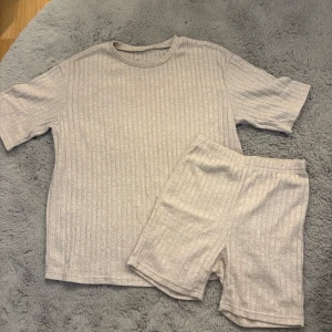 Beige ribbade shorts och t-shirt i mjukt material - Säljer ett par ljusbeige shorts och t-Shirt med ribbad struktur och elastisk midja. De är tillverkade i ett mjukt och bekvämt material, perfekta för chill dagar. Shortsen har en enkel och clean look som är lätt att matcha med allt.