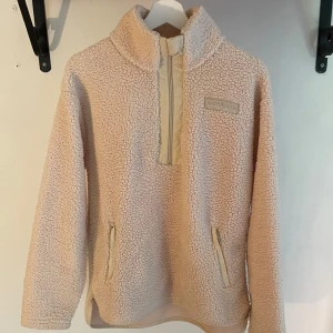 Beige fleece från Norrsken i stl S - Supermjuk och mysig beige fleece från Norrsken med hög krage och half zip framtill. Tröjan har två fickor med dragkedja och är perfekt för kyliga dagar. Oversized fit och långärmad modell som ger en chill och avslappnad vibe.