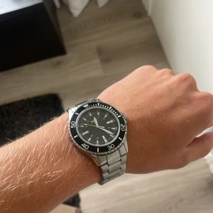 Svart och silver regal klocka - Snygg klocka från regal med svart urtavla och tydliga vita siffror. Klockan har en robust silverfärgad länk i metall och en svart vridbar ring runt urtavlan. Perfekt accessoar för dig som gillar stilren och sportig design. Köptes för nån månad sen men inte använt den något. Pris kan diskuteras 10/10 skick 