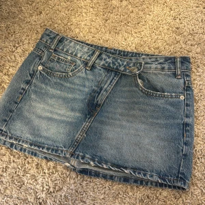 Blå jeanskjol från Zara - Snygg blå jeanskjol från Zara med klassisk femficksdesign, bälteshällor och rå kant nertill. Kjolen är kort och har en avslappnad passform, perfekt till sneakers eller boots. Materialet är slitstarkt denim i bomull.
