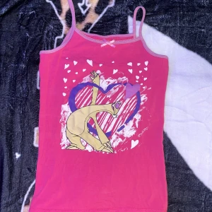 Rosa linne med Sid från Ice Age - Säljer ett rosa linne med smala axelband och en söt liten rosett framtill. Tryck med Sid från Ice Age, hjärtan och ett stort hjärta i bakgrunden. Perfekt för dig som gillar tecknade motiv och färgglada plagg.