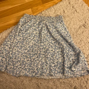 Blommig blå kjol  - Supersöt ljusblå kortkjol från 157 med vitt blommönster och elastisk midja. Kjolen har en flowy passform och är perfekt för vår och sommar. Lätt och skön att bära, passar till sneakers eller sandaler.