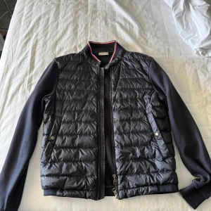 Moncler cardigan  - Säljer min Moncler cardigan eftersom den inte passar mig storleksmässigt. Storlek M men sitter som S. Är en mycket eftertraktad modell som är riktigt snygg och inte säljs längre. Jackan är äkta och köptes på vongreven closet och kvitto finns på det. Det finns 2 små märken på jackan som visas på bild 4 och 5. Ingenting som jag stört mig på då de knappt syns och det kommer inte ut något dun där.  BVSA 