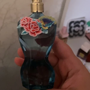 Jean Paul Gaultier La Belle EdT - Parfymflaska i form av en blå kvinnokropp med broderade blommor i rött, gult och blått vid halsen. Flaskan har guldfärgad spraykork och är riktigt snygg som inredningsdetalj också.