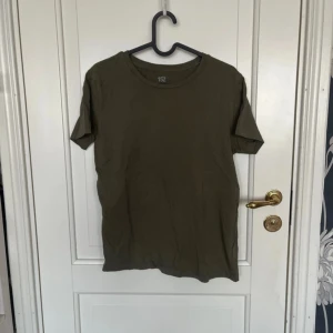 Olivgrön t-shirt från 157, stl S - En basic olivgrön t-shirt från 157 i 100% ekologisk bomull. Klassisk rund halsringning och korta ärmar, perfekt till jeans eller shorts. Enkel och stilren modell som funkar till det mesta.