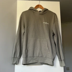 Grå hoodie från Aeuphorie - Snygg grå hoodie från Aeuphorie med vit logga på bröstet. Tröjan har huva, känguruficka och långa ärmar med muddar. Perfekt för en chill och avslappnad stil.
