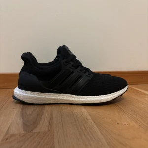 Svarta Adidas Ultraboost - Säljer ett par svarta Adidas Ultraboost med vit boost-sula. Ovandelen är i stickad syntet med klassiska tre ränder på sidan och snörning. Perfekta för dig som gillar stilrena och bekväma skor med sportig vibe. Skorna är i nyskick och är endast testade tveka inte över att höra av dig vid frågor 😁