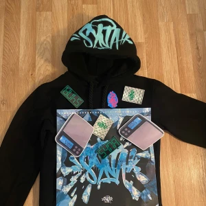 Syna World Hoodie S – Limited Edition Streetwear  - Supersnygg hoodie från Syna World  – extremt ovanlig och svår att få tag på!  Full med detaljer: tryckta digitalvågar, graffiti-taggar, sedelbuntar och fet design framtill och på huvan.  Perfekt skick – oanvänd   Sitter snyggt, normal i passformen  Hype streetwear som garanterat drar blickar 👉Säljer pga garderobsrensning – passa på! 