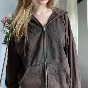 Brun emo y2k hoodiejacka med tryck och dragkedja - Mysig brun hoodiejacka med svart tryck framtill, hel dragkedja och stora fickor. Jackan har huva med snören och en relaxed passform, perfekt för chill dagar. Materialet är mjukt och känns skönt mot huden.