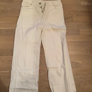 Vita raka jeans från Never Denim - Snygga vita jeans från Never Denim med raka ben och klassisk femficksmodell. Jeansen har hög midja, knäppning med knappar och är tillverkade i kraftig bomull. Perfekta för en clean och stilren look.