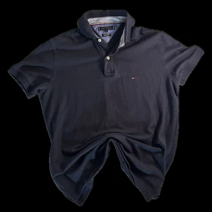 Mörkblå pikétröja Tommy Hilfiger M - Klassisk mörkblå pikétröja från Tommy Hilfiger i bomull med regular fit. Tröjan har korta ärmar, krage med knappar och diskret logga på bröstet. Snygga randiga detaljer på insidan av kragen ger en extra touch. Perfekt för en clean och stilren look.