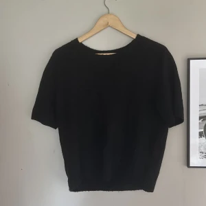 Svart stickad tröja från H&M - En svart stickad tröja från H&M med korta ärmar och rund halsringning. Tröjan har en enkel och clean look, perfekt att styla med jeans eller kjol. Mjuk och skön känsla tack vare det stickade materialet.