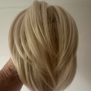 Ny. Blond hårklämma med syntetiskt hår - Snygg blond hårklämma med syntetiskt hår som ger extra volym och längd. Perfekt för att snabbt fixa en cool frisyr. Klämman är ljusbeige och håret har naturliga blonda nyanser. Enkel att fästa och sitter stabilt hela dagen. Hårförlängning/hårbulle. Aldrig använd, längd 21cm.