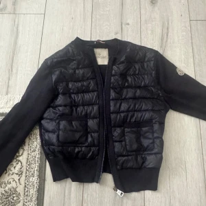 Moncler cardigan dam - Snygg moncler cardigan pufferjacka från Moncler med quiltad framsida och två fickor. Jackan har långärmade stickade ärmar och ribbade muddar. och har klassisk Moncler-logga på ärmen. Perfekt för dig som vill ha en stilren och exklusiv look. Obs : dragkedjan är borta!