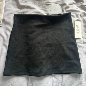 Svart kortkjol från Nelly - Enkel och stilren svart kortkjol från Nelly i figurnära modell. Kjolen har en rak passform och är tillverkad i ett mjukt, stretchigt material som sitter snyggt på kroppen. Perfekt att matcha med en crop top eller oversized hoodie.