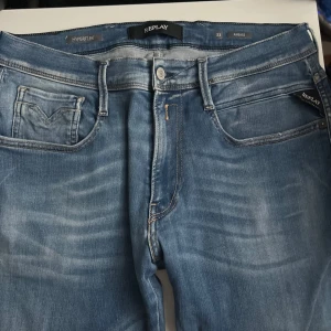 Replay Anbass Hyperflex jeans blå - Snygga Replay Anbass Hyperflex jeans i mellanblå tvätt med diskreta slitningar. Klassisk femficksmodell med stretchigt material för extra komfort. Märkesdetaljer på ficka och bak, samt coola kontrastsömmar. Perfekta jeans för en avslappnad och trendig look. Skriv om du är intresserad eller vill ha mer bilder