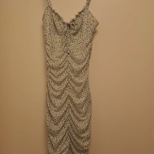 Blommig kortklänning från H&M Divided - Supersöt kortklänning med blommigt mönster i vitt, grönt och blått från H&M Divided. Klänningen har smala axelband, snörning framtill och volangdetaljer vid urringningen. Figurnära passform och rynkade sömmar längs hela klänningen.