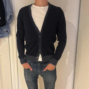 Mörkblå kofta från Stenströms, M - Snygg mörkblå kofta från Stenströms i storlek M. Koftan har knappar framtill, ribbade muddar och kontrastkant i grått. Perfekt för lager-på-lager. Klassisk och stilren design med lång ärm.