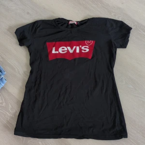 Svart Levi's t-shirt med röd logga - Svart t-shirt från Levi's i storlek 2XL,men liten i storlek, passar till M, L med klassisk röd och vit logga framtill.  T-shirten har rund halsringning och korta ärmar. Perfekt för dig som gillar en enkel men ikonisk streetstil.