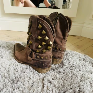 Buffalo Cowboy Boots - Bruna Buffalo cowboyboots med spetsig tå och guldiga nitar. Träklack och sula med bra kvallitet. Köpta secondhand där de använts flitigt men behandlats väl, inte använda av mig eftersom de var för små.🫶🏻