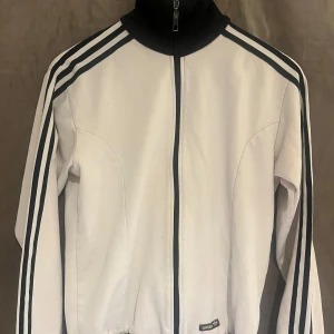 Vit Adidas track jacket med svarta detaljer, Storlek S - Adidas Track Jacket, den har lite fläckar på. Mammas från 2000s så vet inte om fläckarna försvinner!!💖