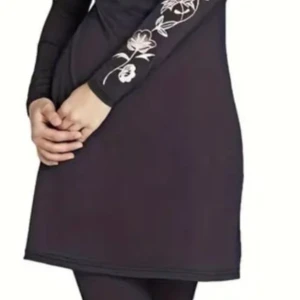 Svart långärmad baddräkt med blommor - Den är XL men M samtidigt Svart kortklänning med lång ärm och vita blommiga broderier på ena ärmen. Klänningen är rak i modellen och gjord i ett mjukt, stretchigt syntetmaterial. Perfekt för dig som gillar enkel men snygg stil med en twist.