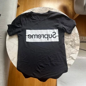 Svart Supreme t-shirt med tryck - Svart t-shirt från Supreme med klassiskt box logo-tryck i vitt över bröstet. Skön passform och rund halsringning, perfekt för dig som gillar streetwear och vill sticka ut med en ikonisk look.