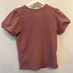Lila topp med puffärm - Säljer en jättegullig mörklila topp från Name It med puffiga korta ärmar och rund halsringning. Toppen är i mjuk bomull och har en enkel, stilren design som passar perfekt till jeans eller kjol. Tröjan är i storlek 146/152 men passar mig som oftast har XS. Skriv om ni har frågor!