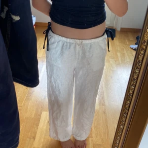 Vita linnebyxor med snörning från H&M - Säljer ett par vita linnebyxor från H&M med elastisk midja och snörning i sidorna. Byxorna har raka ben och två bakfickor för en chill och luftig vibe. Perfekta för varma dagar när du vill ha det bekvämt men ändå stilrent.