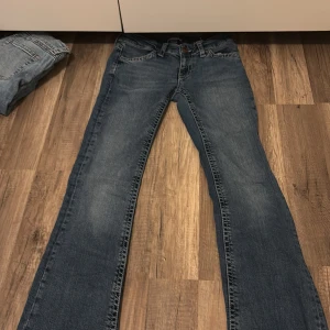 Blå bootcut jeans från Gina Tricot - Snygga blå jeans från Gina Tricot i bootcut-modell. Jeansen har klassisk femficksdesign, markerade sömmar och coola bakfickor med lock och knapp. Tillverkade i jeansmaterial med lätt tvättad look. Perfekta för dig som gillar en avslappnad men trendig stil.