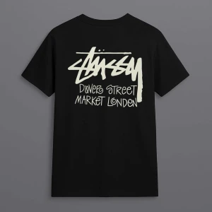 Svart Stüssy t-shirt Dover Street Market - Svart t-shirt från Stüssy med stor vit grafisk logga och texten 'Dover Street Market London' på ryggen. Klassisk passform och korta ärmar, perfekt för dig som gillar streetwear och vill sticka ut med en ikonisk look.