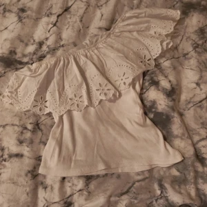 Vit offshoulder topp från Zara - Supersöt vit offshoulder topp från Zara med bred volangkant och broderade blommor. Toppen är ärmlös och har en romantisk känsla med snygga spetsdetaljer. Perfekt för varma dagar och somriga outfits! Passar fint på de som har storlek xxs eller xs