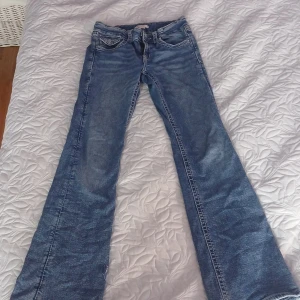 Blå bootcut jeans Gina Tricot 164 - Snygga blå jeans från Gina Tricot i storlek 164. Modellen har bootcut-ben och klassisk femficksdesign. Bakfickorna är dekorerade med broderade detaljer och knappar. Jeansen är tillverkade i mjukt denimtyg och har normal passform.