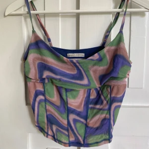 Linnetopp från Urban Outfitters - Färgstark linnetopp från Urban Outfitters med psykedeliskt mönster i lila, grön och rosa. Topp med tunna axelband, croppad passform och markerade sömmar framtill. Står L men mer som en M!!