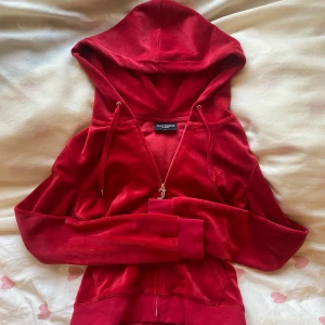 Röd velour hoodie från Juicy Couture - Juicy Couture hoodie i röd velour med dragkedja och huva. Klassisk J-dragkedja, snörning i huvan och kängurufickor framtill. Slim fit och supermjuk, ny känsla. 