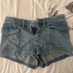 Blå jeansshorts med fickor - Klassiska blå jeansshorts med två stora fickor framtill och bälteshällor. Modellen har normal passform och är tillverkad i denim. Perfekta för varma dagar och enkel att matcha med olika toppar. Oanvända 
