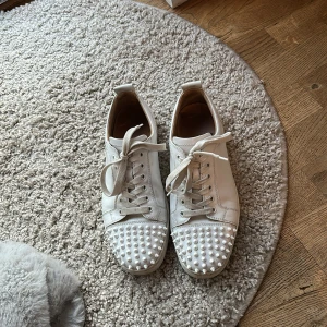 Vita sneakers med nitar från Christian Louboutin - Säljer ett par vita sneakers från Christian Louboutin. Skorna är köpta från Vestiaire clothing med äkthets bevis. Skolåda och extra spikar följer även med. Vid funderingar om pris eller produkten bara skriv 😊. 