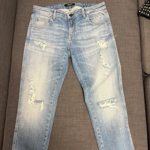 Ljusblå jeans från Replay - Snygga ljusblå jeans från Replay med slitna detaljer för en trendig look. De har en klassisk femficksdesign och knappgylf. Perfekta för en avslappnad stil.