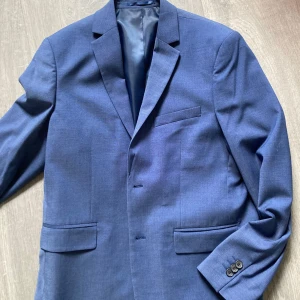 Blå kavaj från Cubus - Snygg blå kavaj från Cubus, perfekt till skolavslutningen och sommarens fester. Kavajen har en klassisk design med två knappar framtill och fickor med lock. Den är tillverkad i ett stilrent material som ger en elegant look. Mycket fin blå färg. 