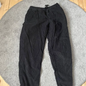 Svarta manchesterbyxor från Vans - Säljer ett par svarta manchesterbyxor från Vans i storlek medium. Byxorna har en elastisk midja med snörning för extra komfort. Perfekta för en avslappnad stil.