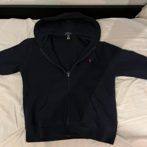 Polo Ralph Lauren zip hoodie - Säljer en snygg mörkblå hoodie från Polo Ralph Lauren med dragkedja och klassisk logga på bröstet. Tröjan har långa ärmar och en praktisk huva. Perfekt för en avslappnad stil. Storlek XL i barn så typ XS-S vanlig storlek