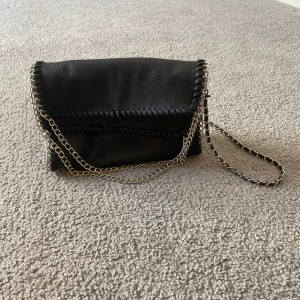 Svart axelväska med kedjerem Gina tricot  - Säljer en svart axelväska med snygga silverfärgade kedjedetaljer och kedjerem säljer den då den inte används. Väskan har en mjuk struktur och stängs med magnetlås. Invändigt finns ett fack med dragkedja. Perfekt för att bära det viktigaste och ge outfiten en cool touch. Väskan är från Gina tricot och säljs inte längre. Nypris 330 kr ❤️tryck gärna köp nu ❤️