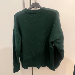 Mörkgrön stickad tröja - Säljer en mysig mörkgrön stickad tröja med långa ärmar. Perfekt för kyligare dagar och enkel att matcha med olika outfits.