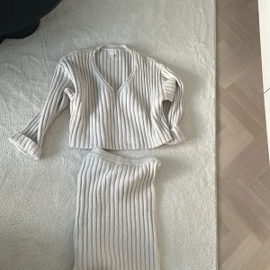 Beige ribbad tröja och kjol set - Säljer ett snyggt set med en beige ribbad tröja och matchande kjol. Tröjan har en v-ringad design och trekvartsärmar, perfekt för en stilren look. Kjolen är i samma ribbade material och ger en enhetlig stil. Tröjan är i M och kjolen i XS då den är väldigt stor i storlek, 