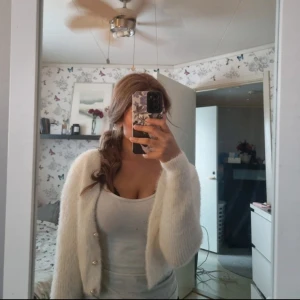 Vit fluffig kofta med pärlknappar - Säljer en supermjuk och fluffig vit kofta med pärlknappar. Perfekt för att hålla sig varm och stilren. Koftan har långa ärmar och en klassisk design som passar till många olika outfits.