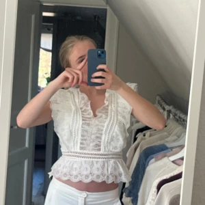 Vit spetsblus - Säljer en vacker vit spetsblus med volangdetaljer och korta ärmar. Blusen har en v-ringad design och är croppad med ett fint spetsmönster. Perfekt för en somrig look! Har kvar prislappen!