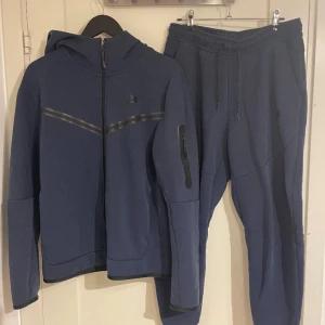 Nike Tech tracksuit mörkblå - Blå Nike Tech Fleece Track Suit – Mjuk & Stilren Säljer min blåa Nike Tech Fleece tracksuit i bra skick! Superbekväm och snygg, perfekt för både vardag och chill. Fleecen och byxorna är i fint skick – dragkedjor, passform och färg är som de ska. Enda minuset är att tyget är lite knoppigt i baksida av byxorna, men inget som syns mycket eller stör användningen. Köptes i Nike i mall of scandinaivia för 2 år sedan för cirka 2200kr. Säljer den för att stillen är inte min favo längre.