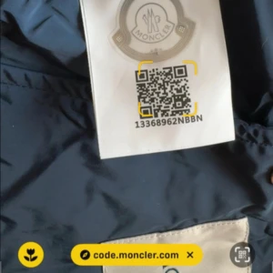 Marinblå vindjacka från Moncler - Säljer en Marinblå vindjacka från Moncler med huva och broderad logotyp på ärmen. Jackan har dragkedja och en diskret röd-vit detalj på huvan. Perfekt för blåsiga dagar och snygg till streetwear. Storlek 2. kvitto finns. (Äkta) Nfc funkar